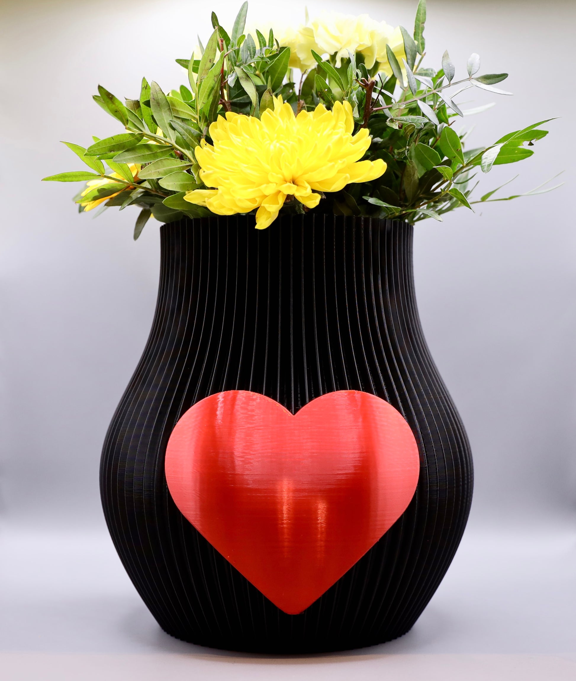 Schwarze 3D-gedruckte Designvase von Wälder Create mit rotem Herzmotiv, dekoriert mit Blumen – gefertigt im Bregenzerwald.