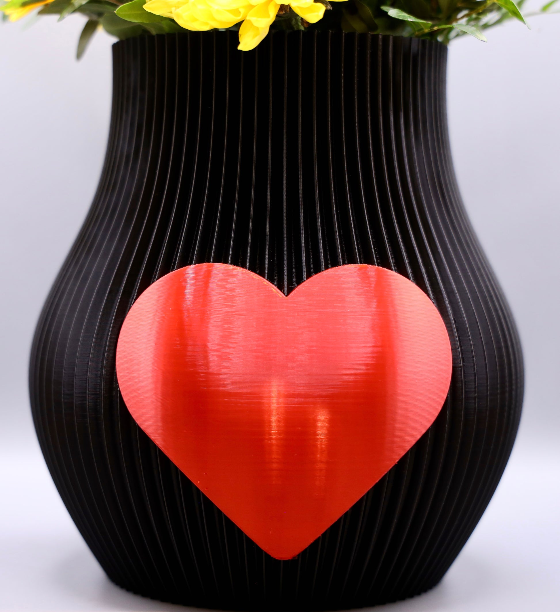 Schwarze 3D-gedruckte Designvase von Wälder Create mit rotem Herzmotiv, dekoriert mit Blumen – gefertigt im Bregenzerwald.