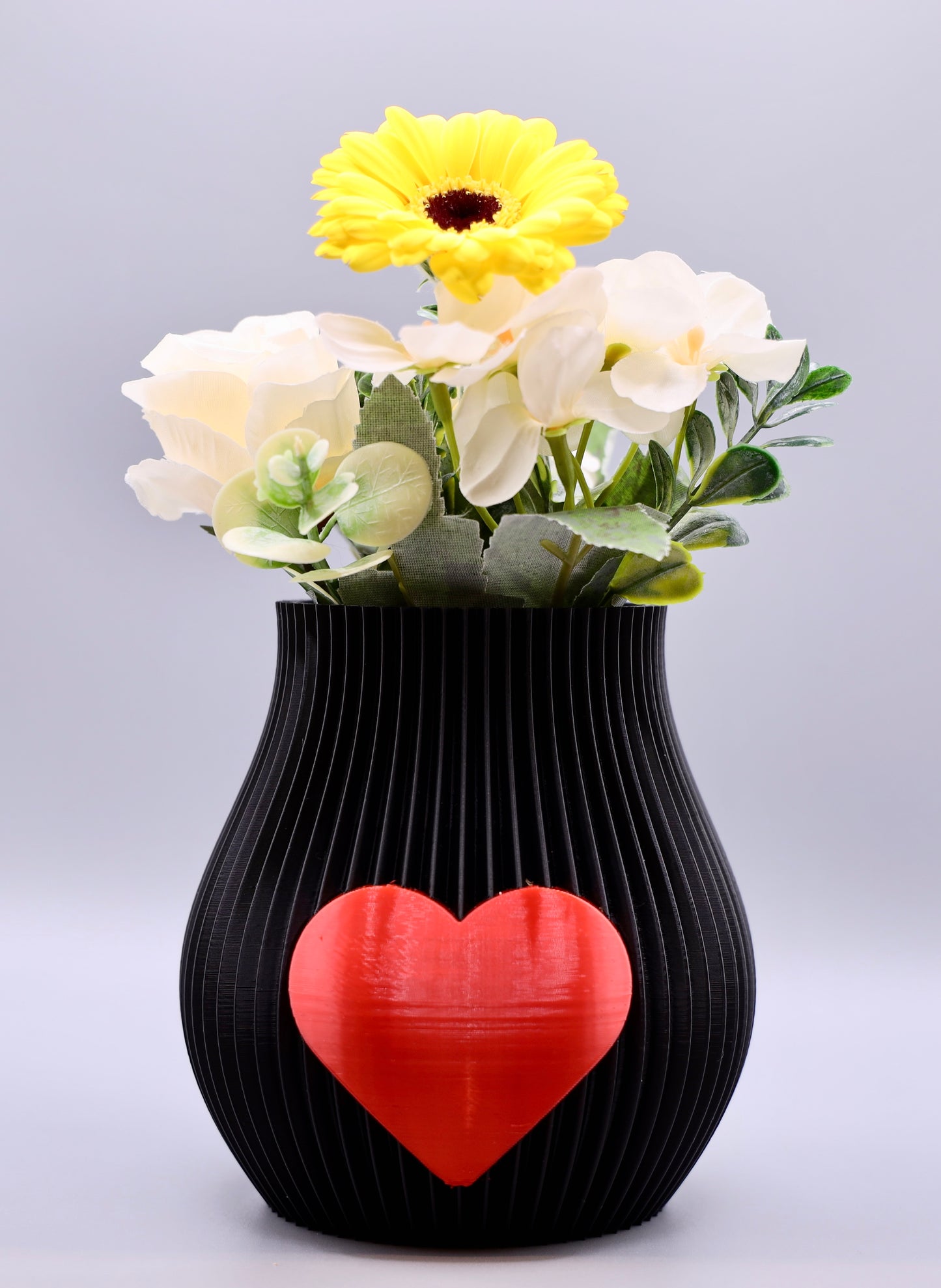 Schwarze 3D-gedruckte Designvase von Wälder Create mit rotem Herzmotiv, dekoriert mit Blumen – gefertigt im Bregenzerwald.