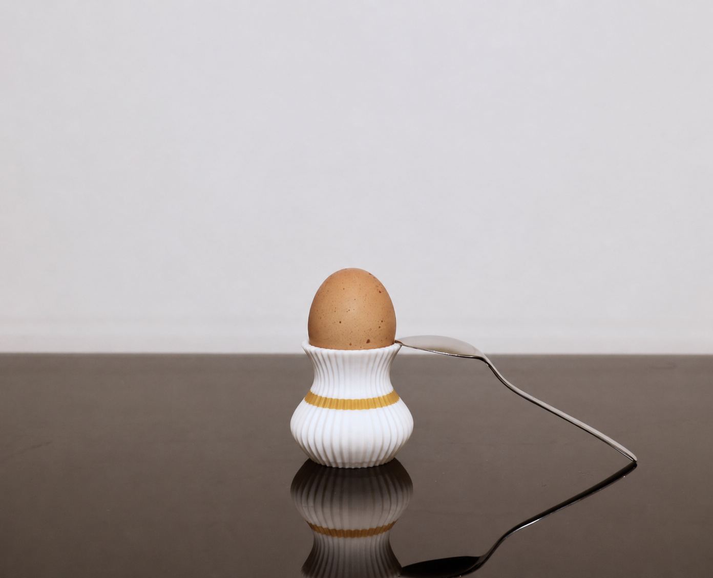 Moderner weißer 3D-gedruckter Eierbecher mit goldenem Akzent, Ei und Löffel als stilvolle Frühstücksdekoration.