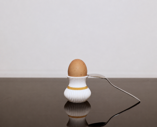 Moderner weißer 3D-gedruckter Eierbecher mit goldenem Akzent, Ei und Löffel als stilvolle Frühstücksdekoration.